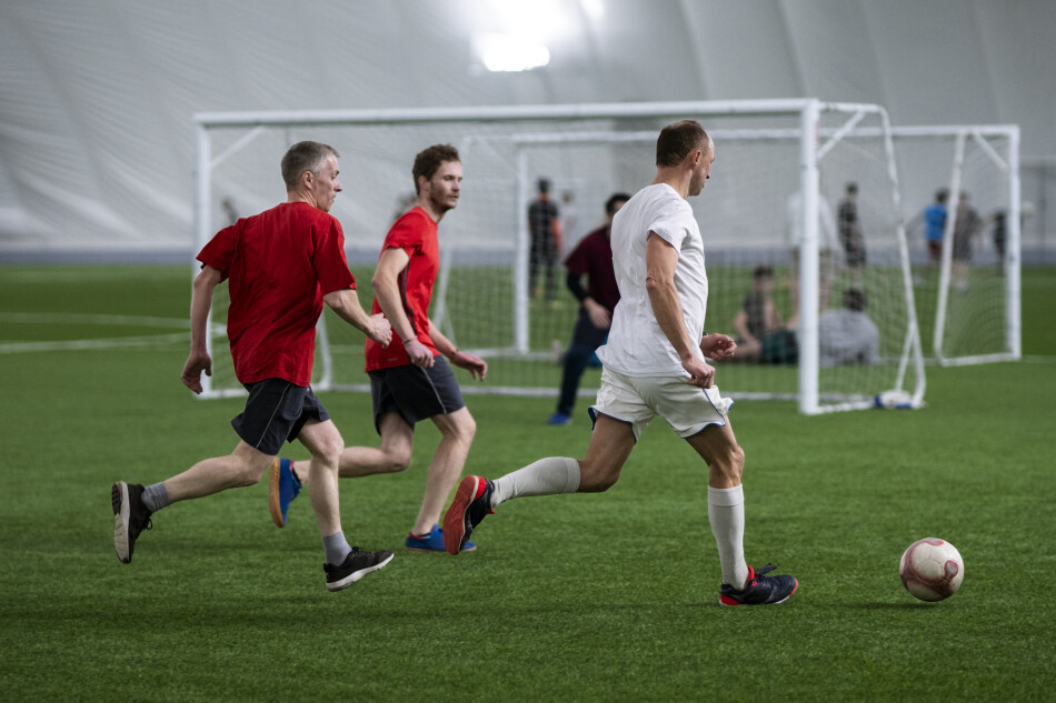 3 trabajadores jugando futbol en una cancga cerrada, disfrutando de un ambiente deportivo
