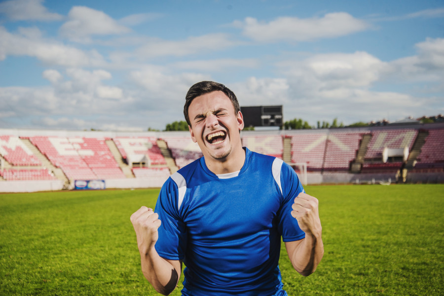 joven con una playera deportiva azul festejando un gol en una cancha de futbol