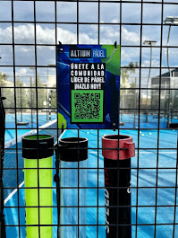 Detalle de la reja de una cancha de pádel con un cartel invitando a unirse a la comunidad y la pista azul de fondo